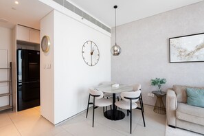 A modern kitchen with a built-in refrigerator, a dining area with a round table and chairs, and a living area with a sofa and a plant.