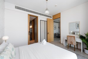 A modern hotel room with a bed, a desk, a chair, and a potted plant. - Cozy Address JBR 1BR w/ Beach Access (Dubai)