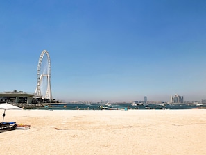 A beach with a Ferris wheel in the background and boats on the water.