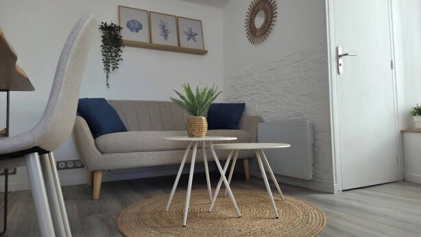 Un salon moderne avec un canapé gris, un tapis rond en fibres naturelles, une petite table blanche et un élément décoratif mural.