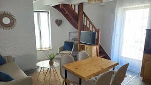 Un salon moderne avec une table à manger en bois, des canapés beiges, un téléviseur posé sur un meuble en bois et un escalier menant à un niveau supérieur.