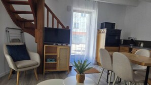 Un salon moderne avec un canapé, deux petites tables, un téléviseur et un escalier.