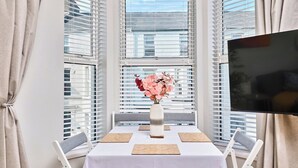 Un comedor con una mesa dispuesta para dos personas, un florero con flores y un televisor montado en la pared.