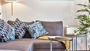 Una sala moderna con un sofá gris, cojines estampados, una mesita auxiliar y una planta en maceta.