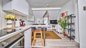 A modern kitchen with a central island, a dining area with a sofa, a TV, and a plant shelf. - Central Portrush Penthouse Retreat (Portrush)