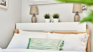A neatly made bed with white and green striped pillows, a white headboard, and two wall-mounted lamps. - Central Portrush Penthouse Retreat (Portrush)