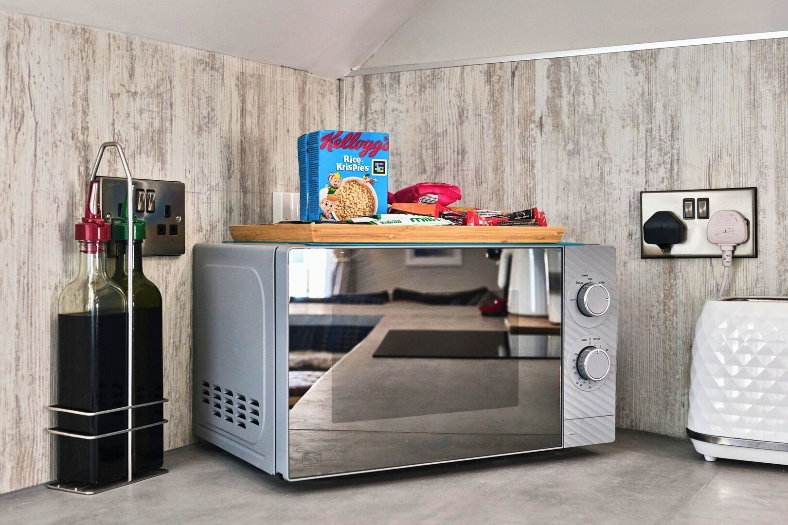 A compact kitchenette with a microwave, a small fridge, and a bottle of olive oil on the counter.