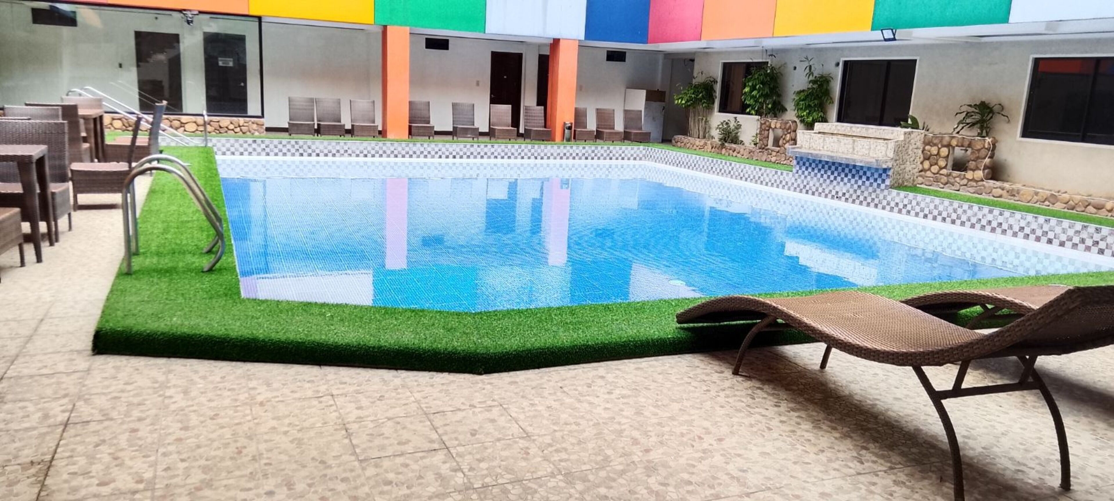Uma piscina com borda quadriculada, rodeada por cadeiras de descanso e piso de azulejos.