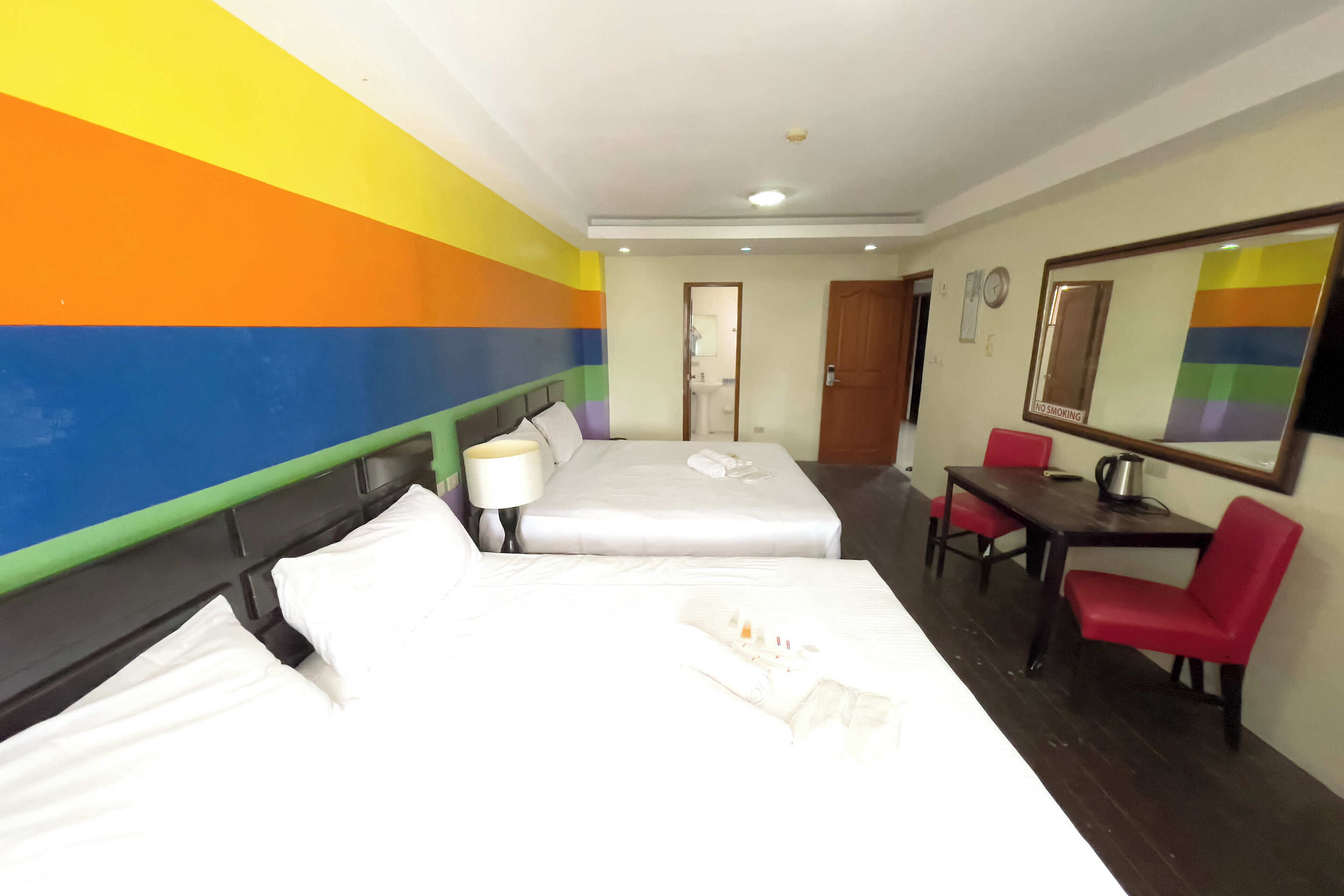 Una habitación de hotel con cama, escritorio, silla, lámpara y espejo.