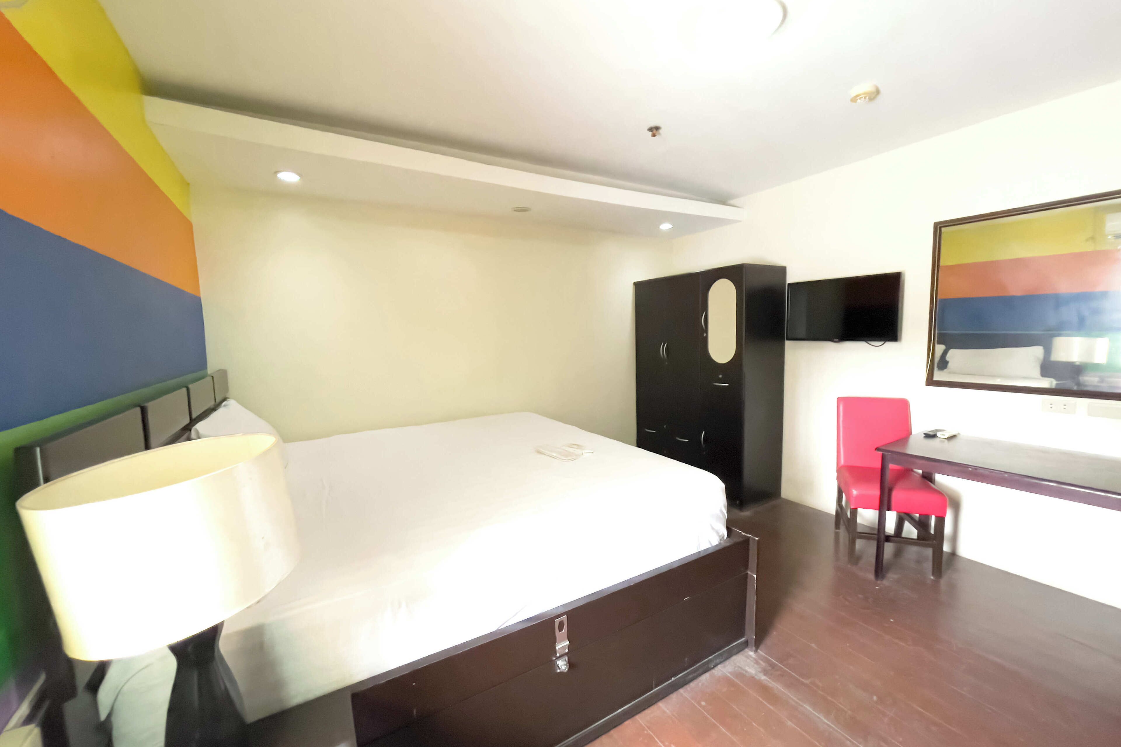 A hotel room with a bed, a desk, a chair, a wardrobe, and a TV on the wall.