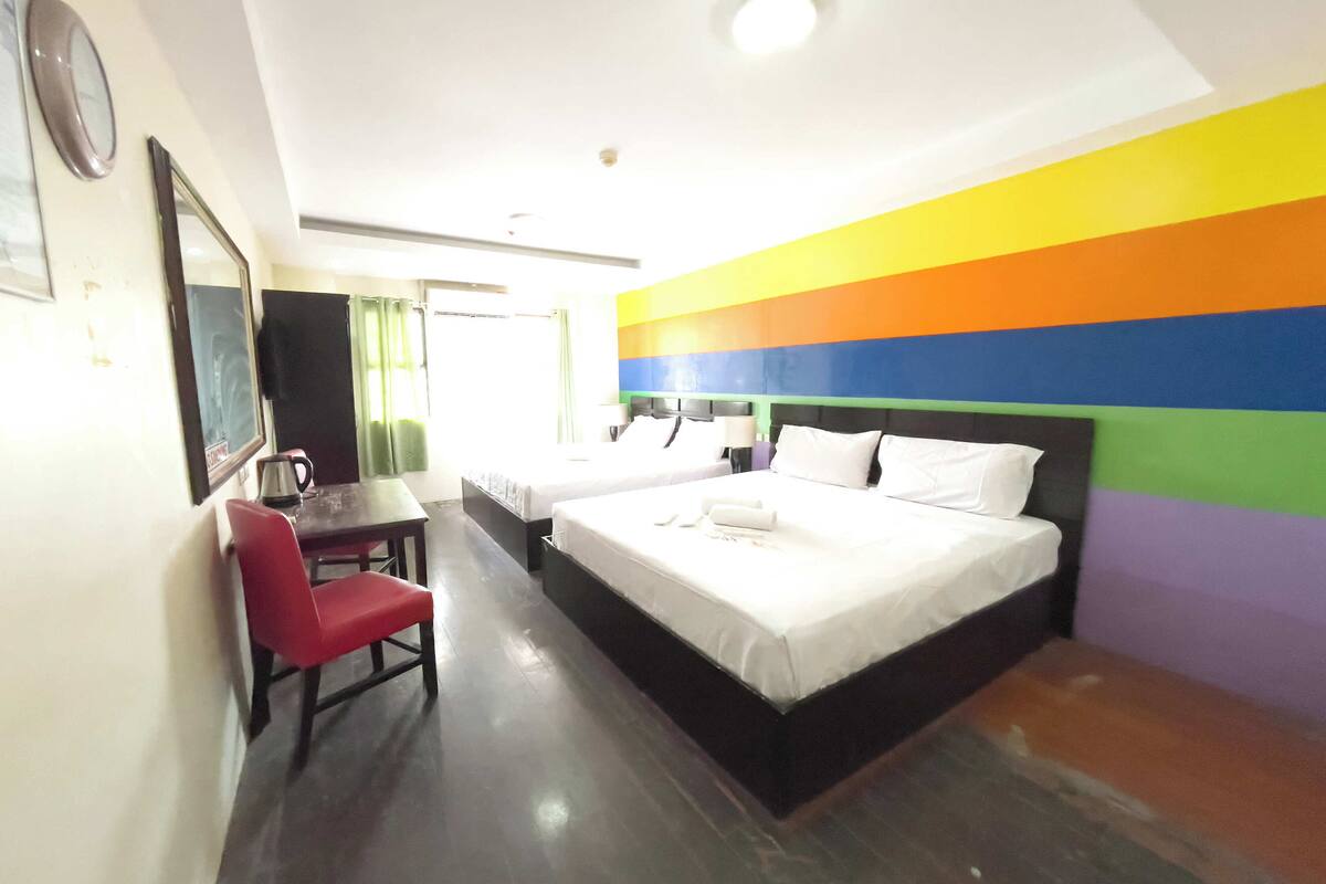Quarto de hotel com cama, escrivaninha, cadeira e parede com um design listrado colorido.