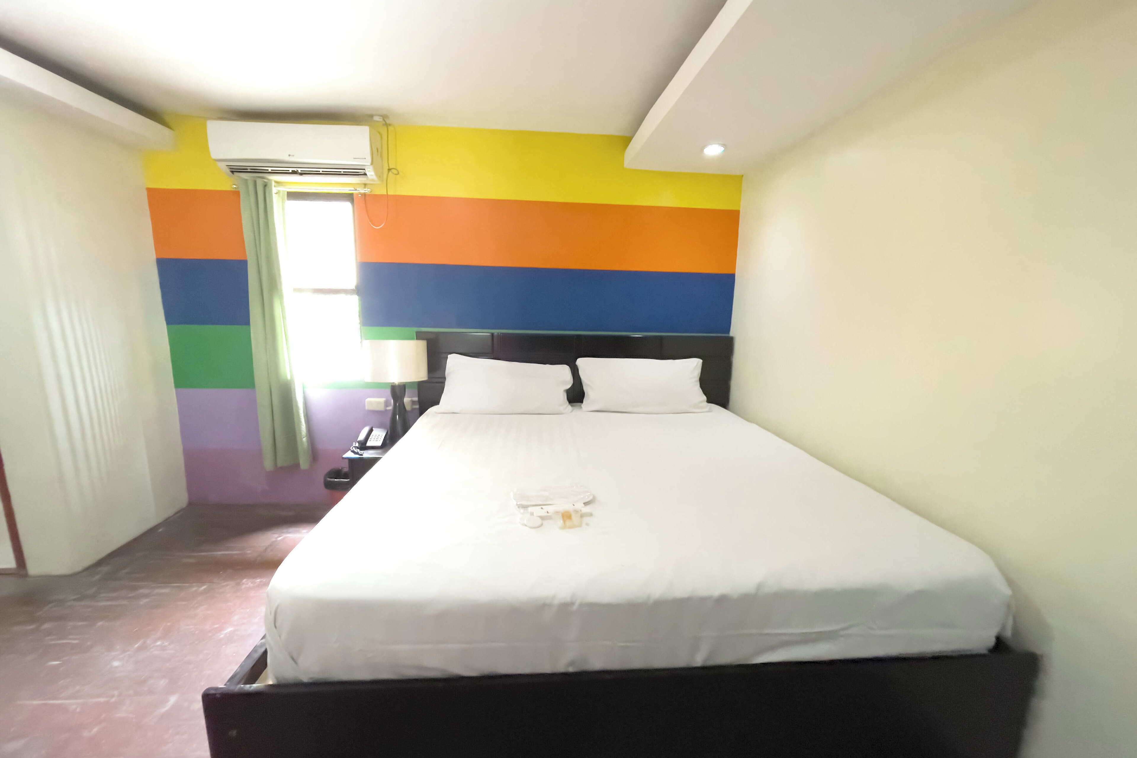 A hotel room with a bed, a nightstand, and a window with curtains.