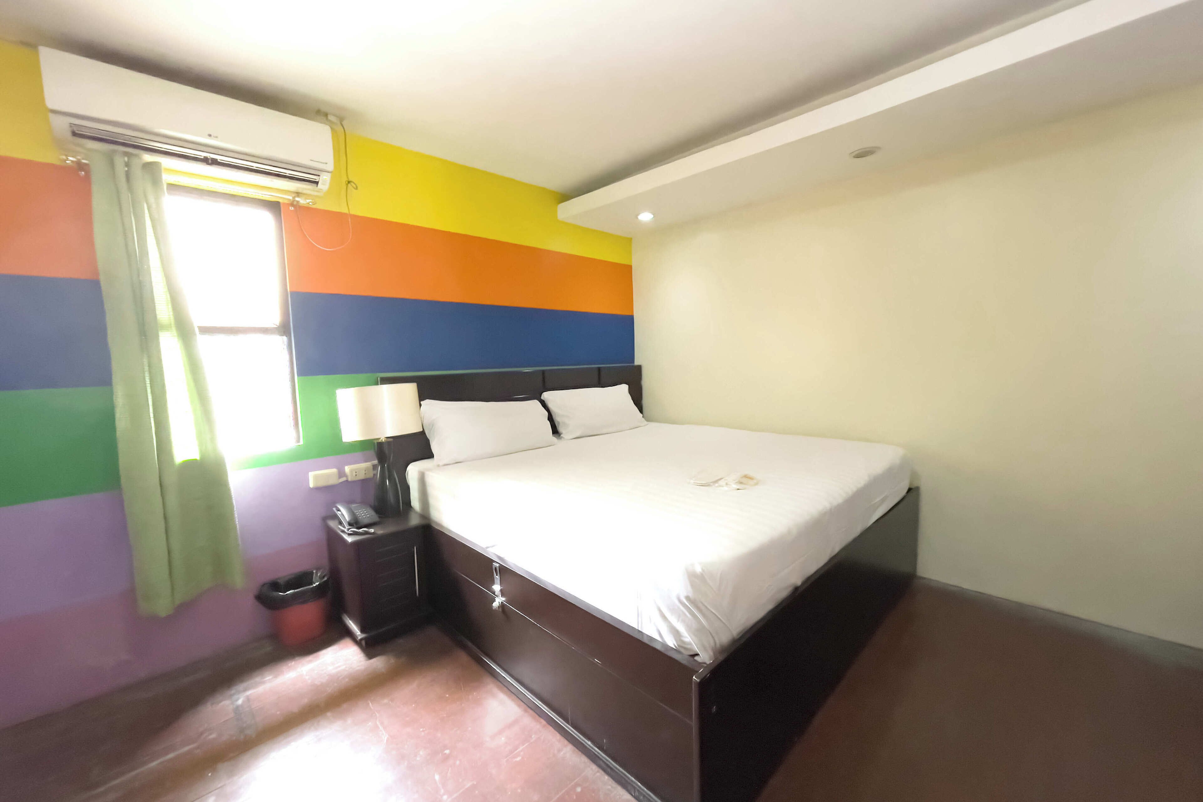 Une chambre à coucher avec un lit, une table de chevet, une lampe et une fenêtre avec des rideaux.
