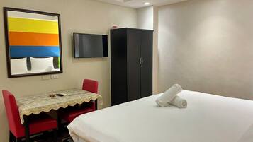 Una habitación de hotel con cama, escritorio con silla, televisor y armario.