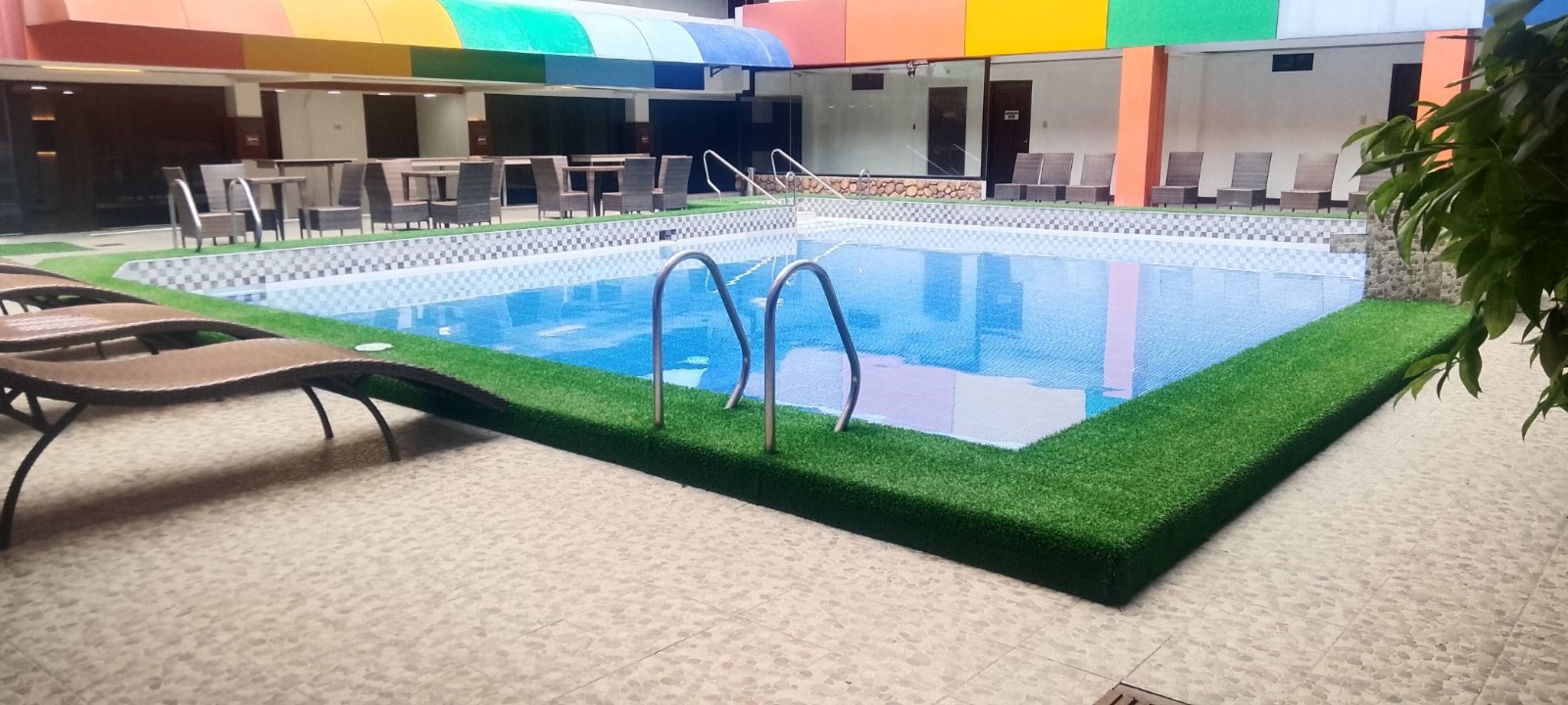 Piscina interna com chão quadriculado, cercada por espreguiçadeiras e um teto colorido.