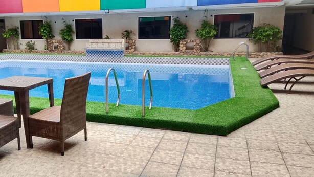 A swimming pool with a checkered border, surrounded by green artificial grass and a tiled deck. - Fave Hotel Angeles City formerly Hotel America (Angeles City)
