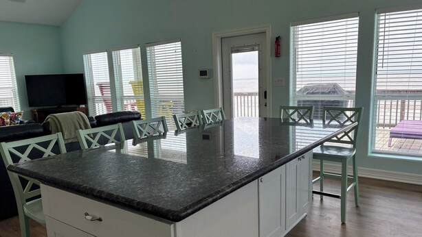 A kitchen with white cabinets, a granite countertop, and a dining area with green chairs.