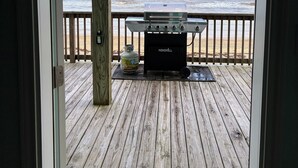 A wooden deck with a grill and propane tank, overlooking a beach.