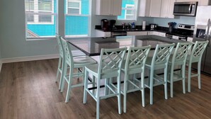 A kitchen with a central island, white cabinets, and a dining area with light green chairs.