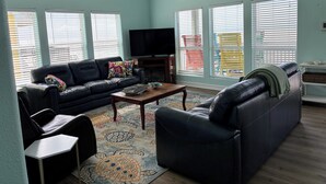 A living room with a black leather sofa, a coffee table, and a flat-screen TV.