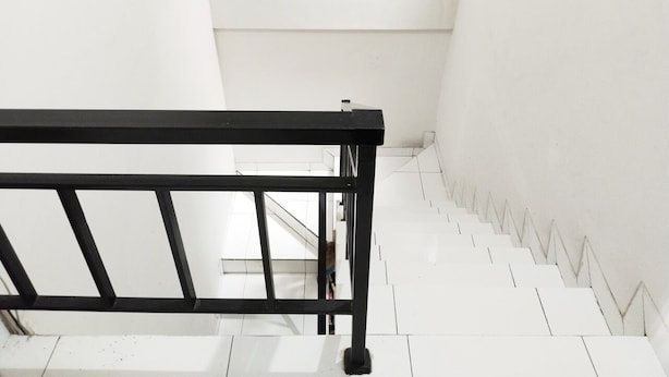 A staircase with a black metal railing and white walls. - Colombus Homy Syariah (Karawang)