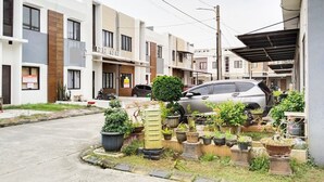 A residential street with modern houses, a parked car, and potted plants along the sidewalk. - Colombus Homy Syariah (Karawang)