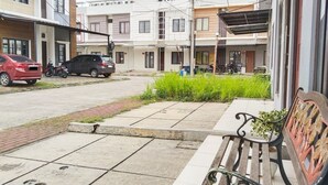 A residential street with parked cars, a bench, and a row of houses. - Colombus Homy Syariah (Karawang)