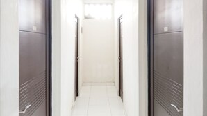 A narrow, well-lit hallway with two doors on either side, leading to a room with a large window at the end. - Colombus Homy Syariah (Karawang)