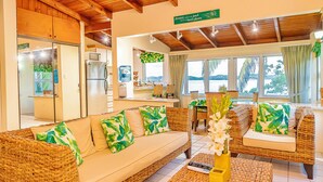 A cozy living area with wicker furniture, a kitchen in the background, and a view of the sea. - Breeze by the sea (St. Johns)