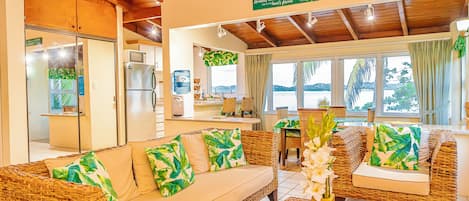 A cozy living area with wicker furniture, a kitchen in the background, and a view of the sea.