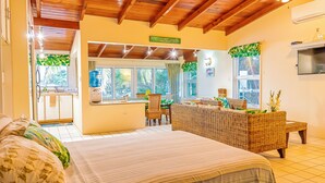 A well-lit room with a bed, a wicker sofa, and a dining area. - Breeze by the sea (St. Johns)