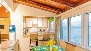 A compact kitchen with a dining area, a water dispenser, and a view of the sea through large windows. - Breeze by the sea (St. Johns)