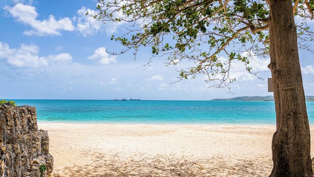 A beach with clear turquoise water, a sandy shore, and a distant ship. - Breeze by the sea (St. Johns)