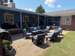 A covered patio area with outdoor furniture, a grill, and a brick wall.