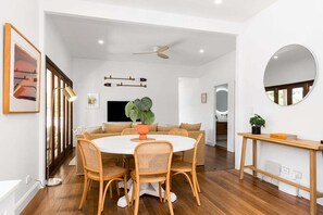 Uma área de refeições moderna com uma mesa redonda, cadeiras de vime, um vaso de planta e um ventilador de teto.