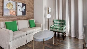 A living room with a sofa, a round coffee table, and a plaid armchair. There are two framed pictures on the wall. - Charming 2-bedroom resort Located at Studio Ellis Square Savannah Georgia (Savannah)