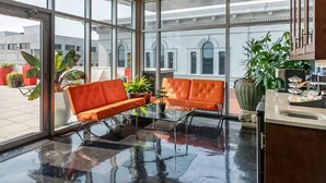 A spacious indoor area with large windows, a glass table, orange seating, and potted plants. - Charming 2-bedroom resort Located at Studio Ellis Square Savannah Georgia (Savannah)