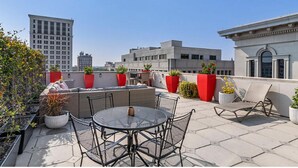 A rooftop terrace with a round table and chairs, potted plants, and a red sofa. - Charming 2-bedroom resort Located at Studio Ellis Square Savannah Georgia (Savannah)