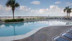 A swimming pool with lounge chairs and palm trees, surrounded by a fence and a clear sky. - Lighthouse Condo 717-King Bed, Queen Sleeper, Twin Bunk Beds, 2 bath, sleeps 6 (Gulf Shores)