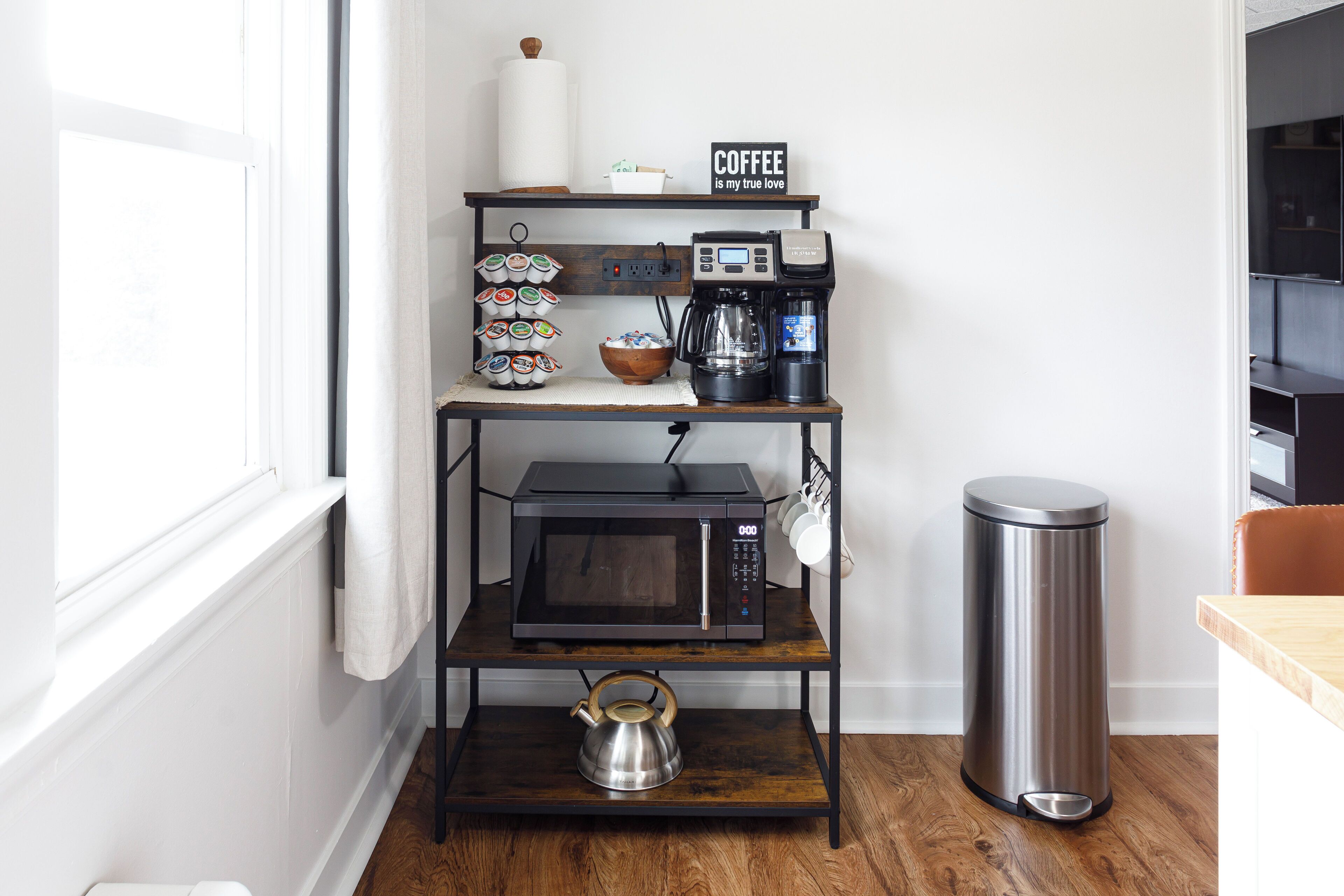A kitchen with a coffee machine, microwave, kettle, and trash can on a wooden shelf unit.