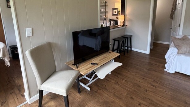 A living room with a TV on a wooden stand, a white chair, a small table, and a sofa.