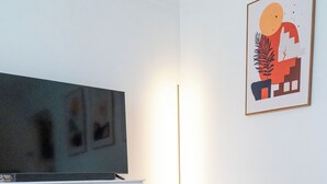 A modern living room with a flat-screen TV, white furniture, and a patterned rug. - 18 min. to Detroit center - free parking on fenced premises (Ecorse)
