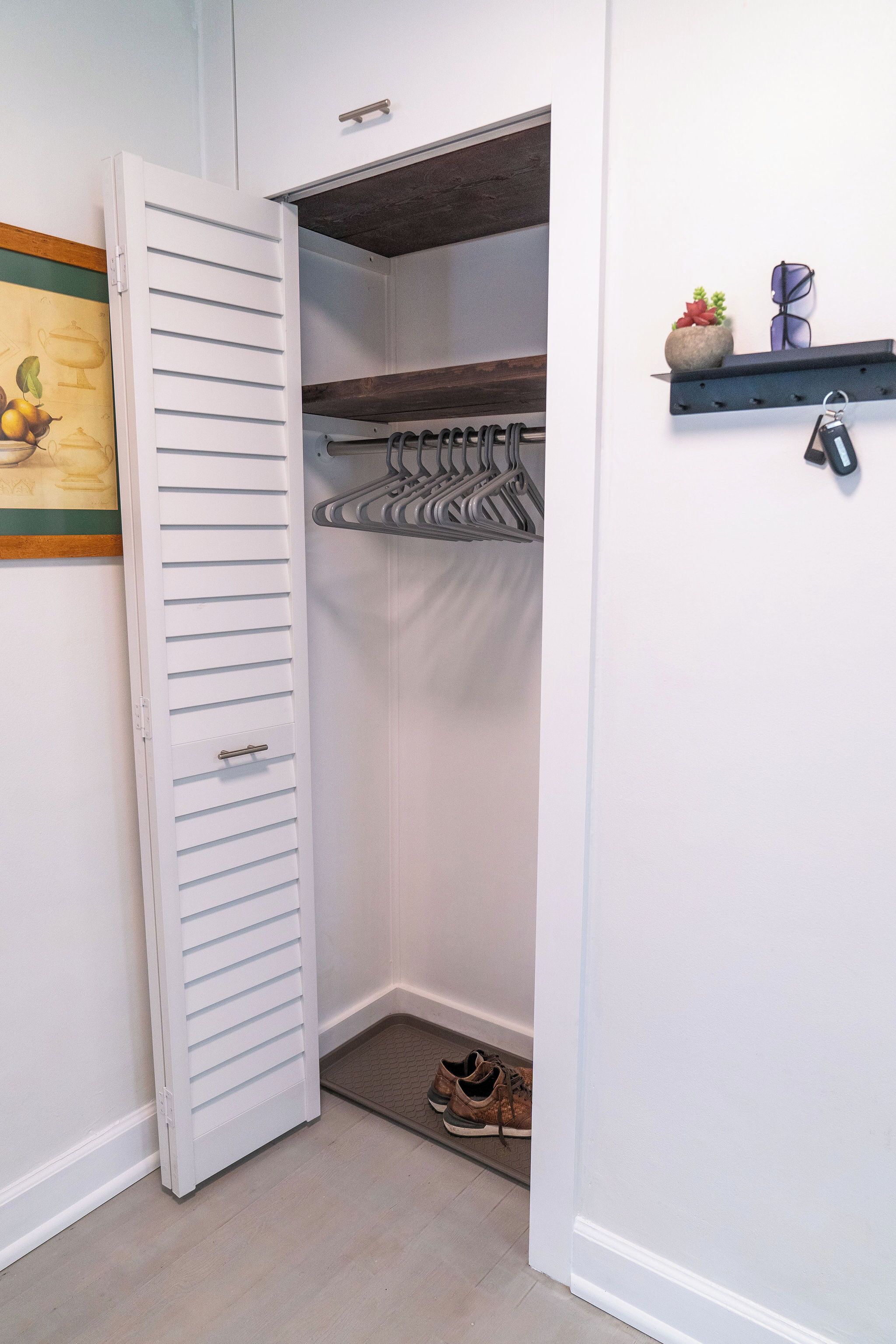Un dressing avec une porte blanche, un porte-chaussures et une petite étagère où sont disposés des objets décoratifs.