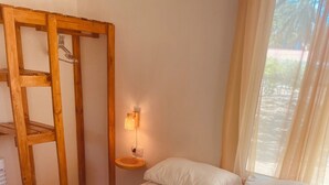 A neatly made bed with white linens, a wooden nightstand with a lamp, and a window with sheer curtains. - Charming 2-bedroom cottage in beautiful Masaya with AC, WiFi (Masaya)