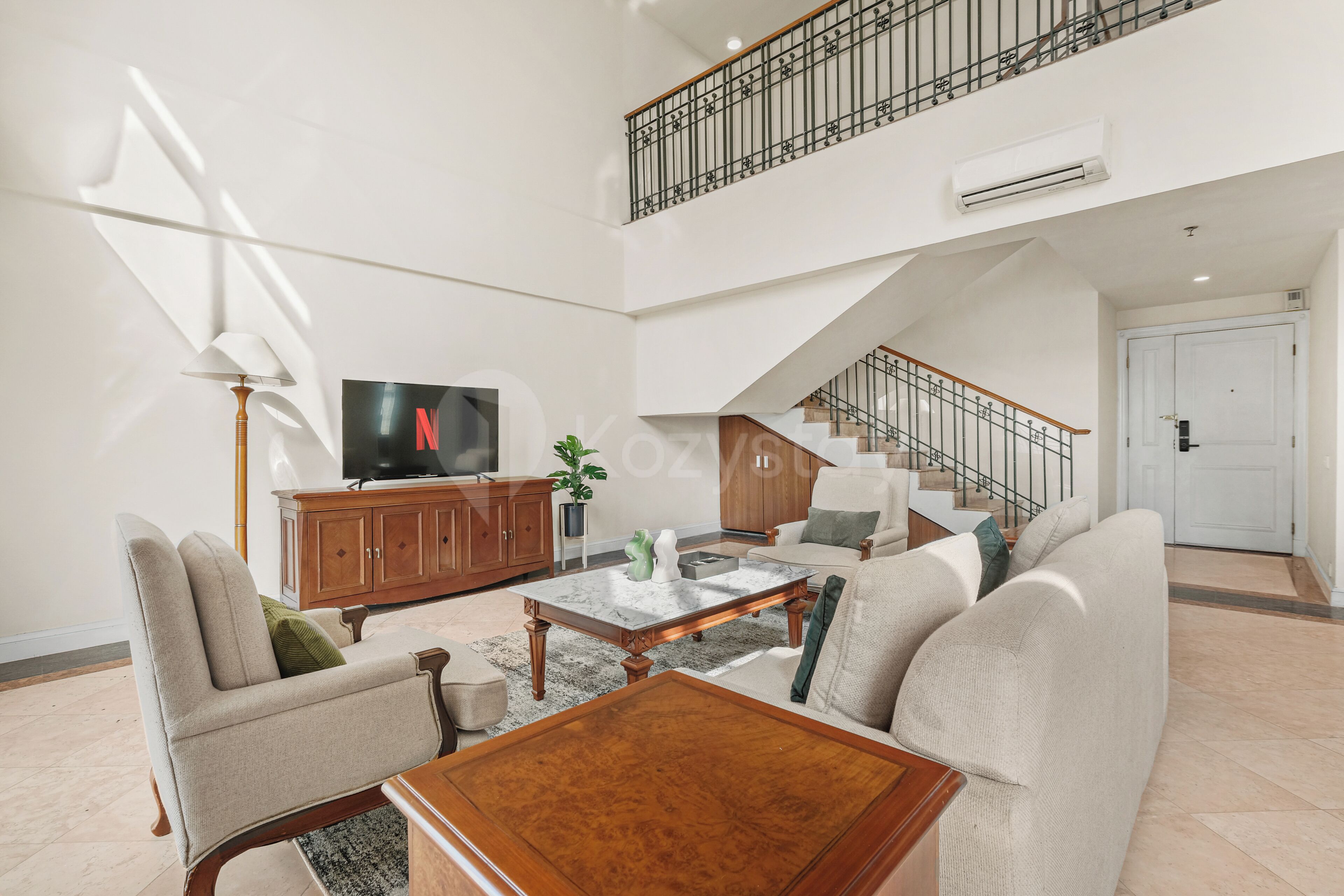 A spacious living area with a high ceiling, a staircase, and a television.