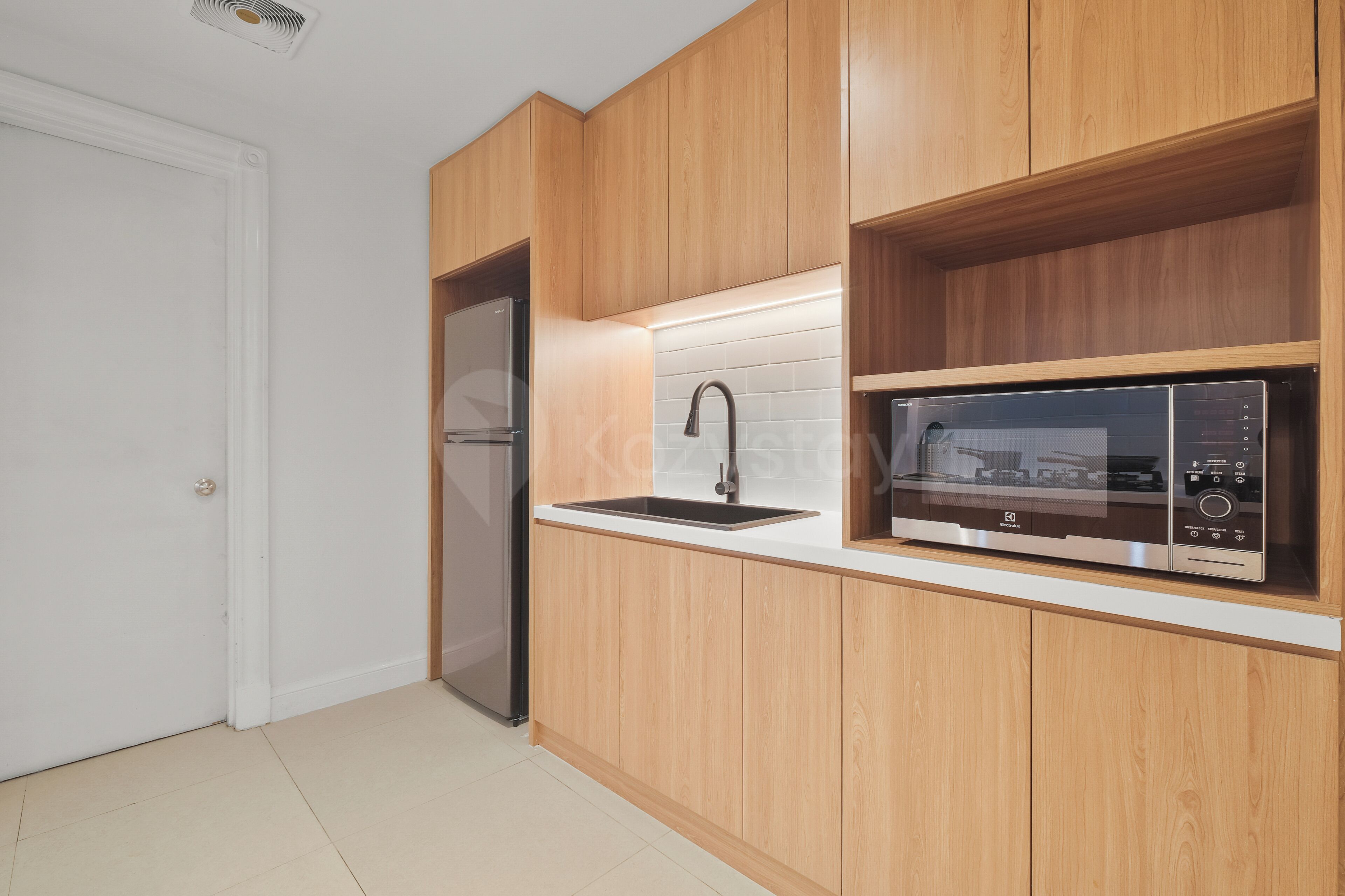 A kitchen with wooden cabinets, a stainless steel refrigerator, a microwave, and a sink.