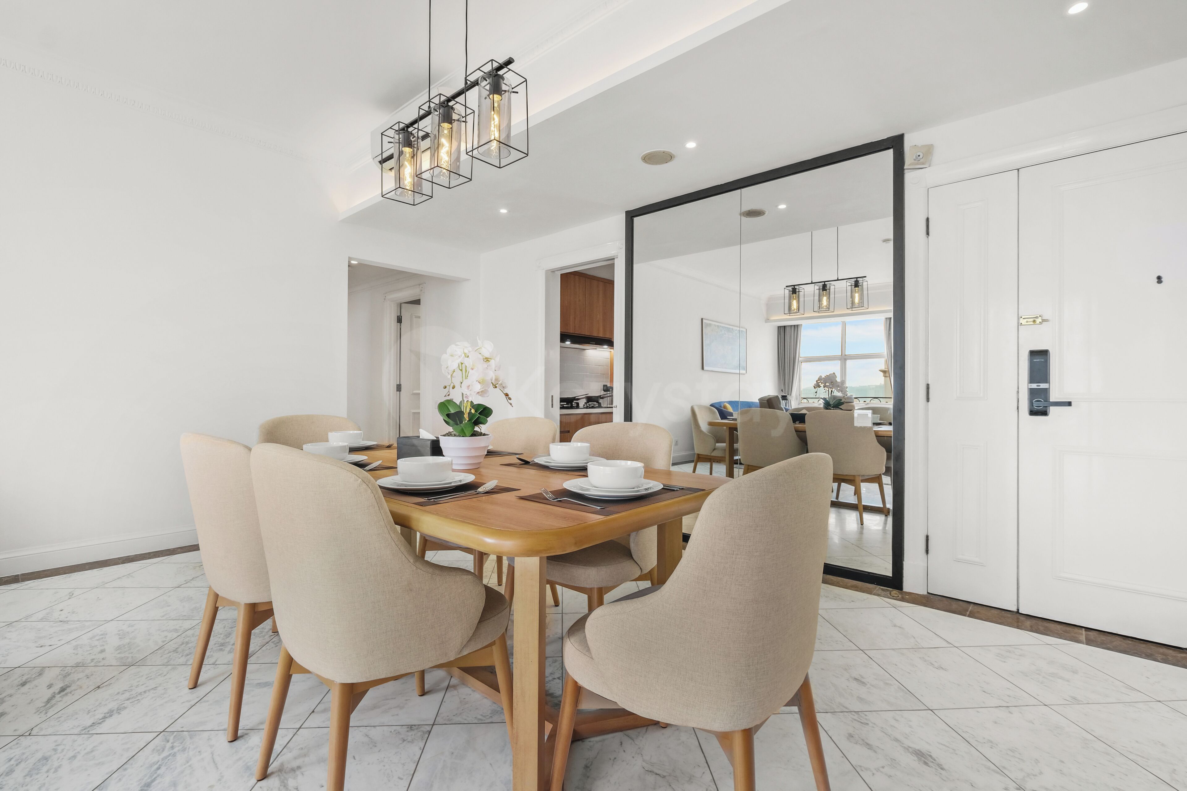 Un espace repas moderne avec une table en bois et des chaises de couleur beige, une plante en pot et une cuisine en arrière-plan.