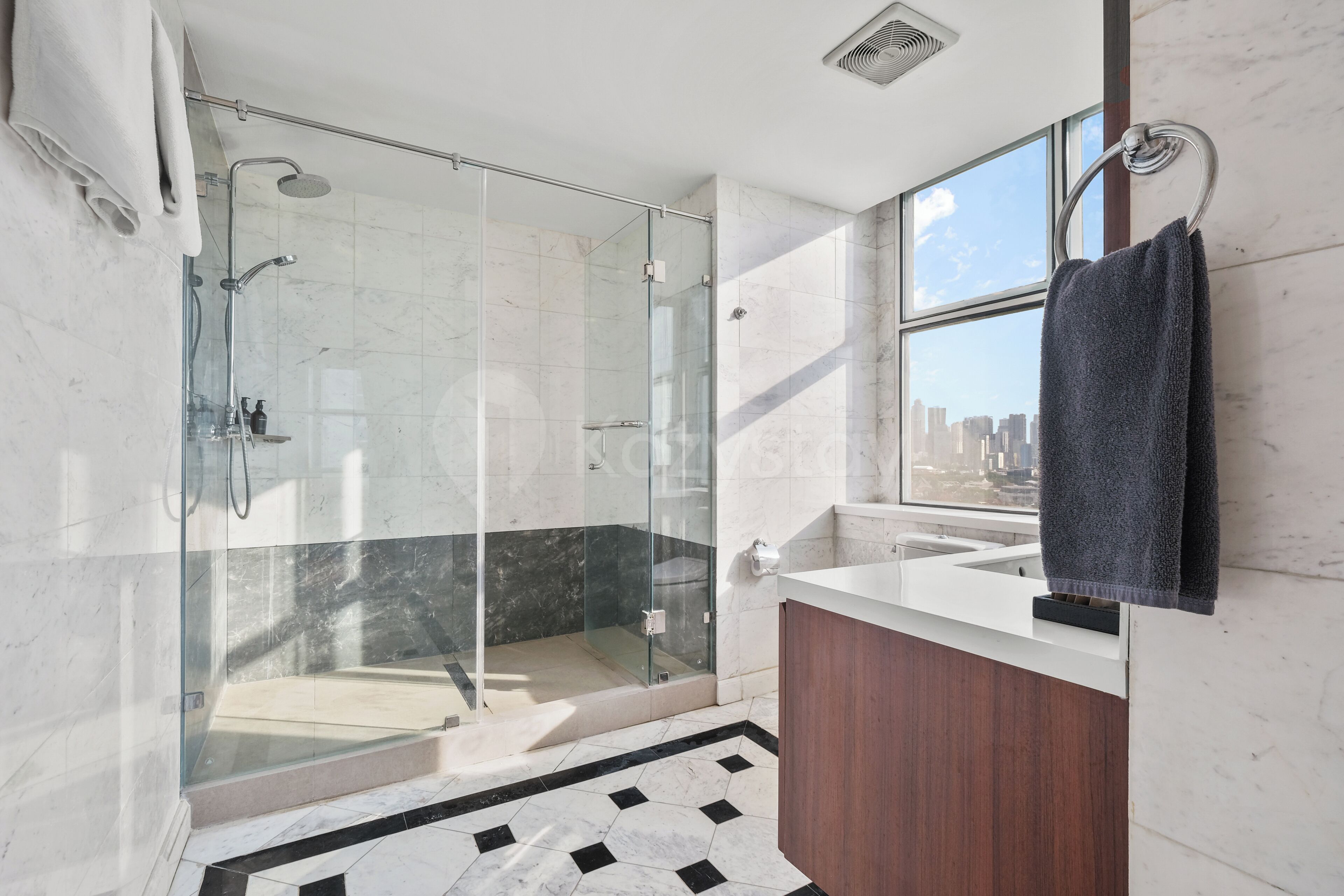 Un baño moderno con ducha envuelta en vidrio, tocador de madera y una ventana grande que ofrece vistas a la ciudad.