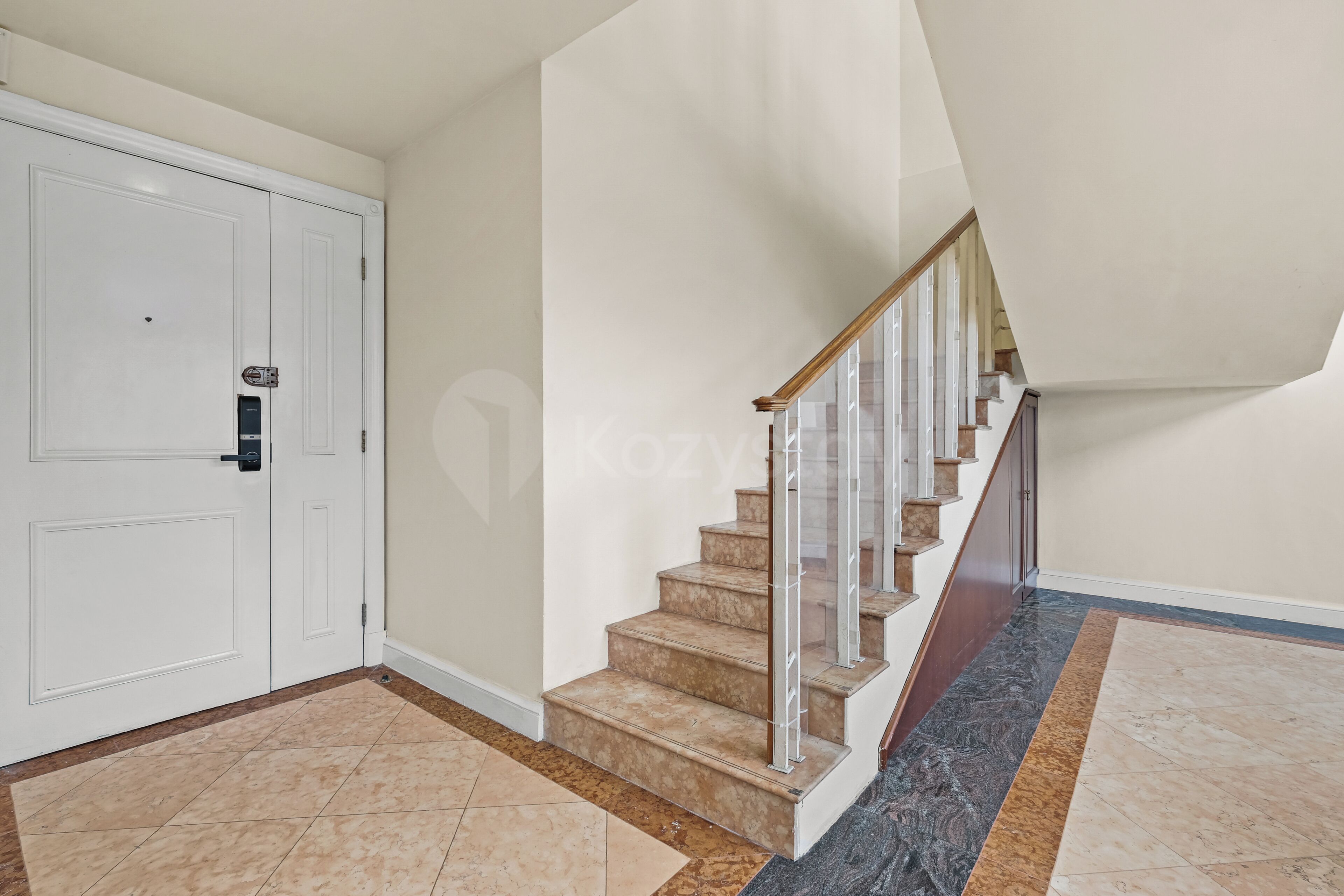 A staircase with a wooden handrail and beige steps, leading to a landing with a white door.