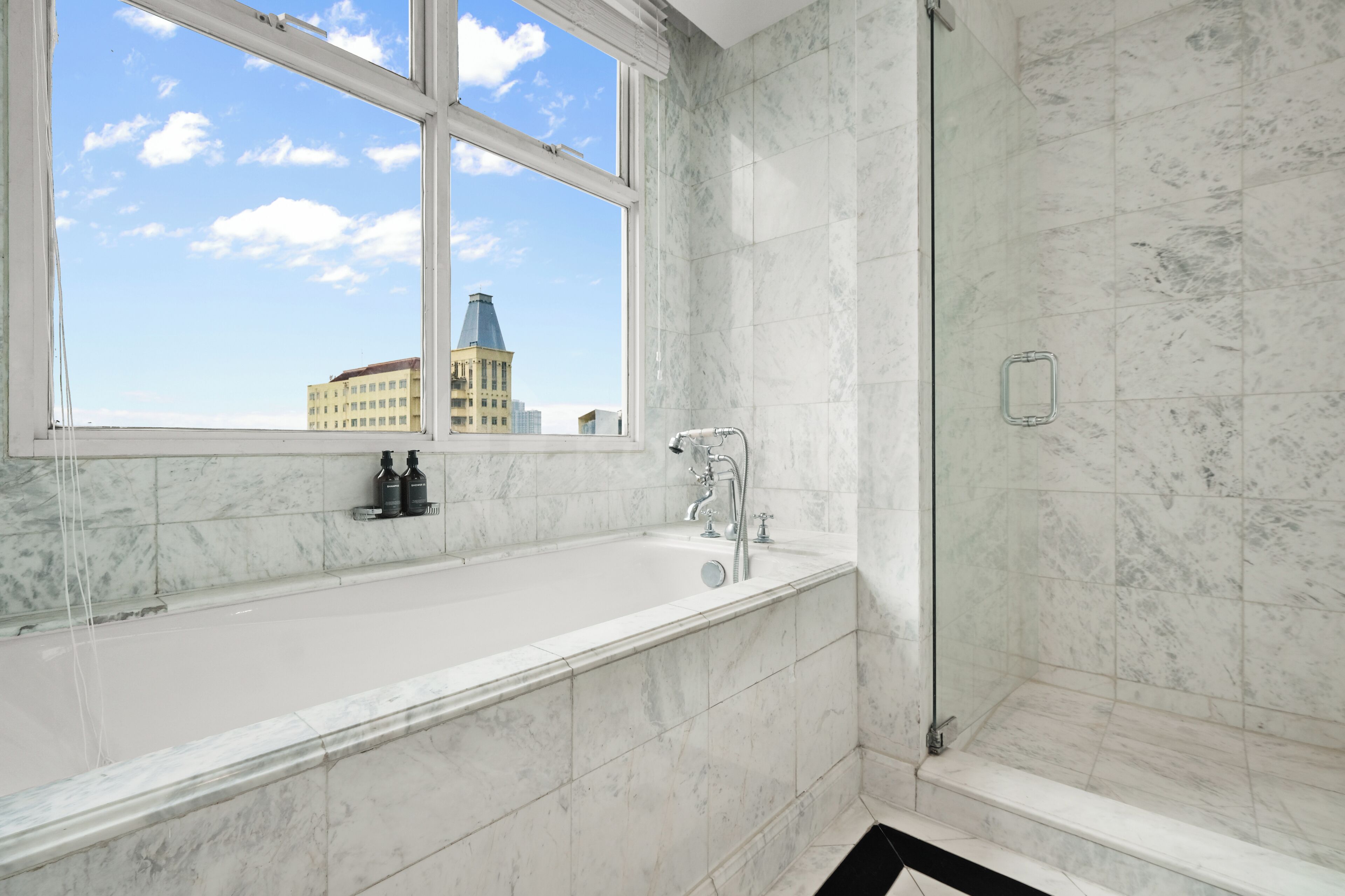 A bathroom with a bathtub, a shower, and a window with a city view.